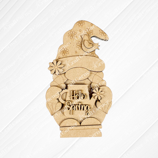 The Hellp Spring Girl Gnome Shelf Sitter by Janet's Craft Corner, a DIY seasonal home decor craft kit, features a wooden girl gnome with a floral hat holding a "Hello Spring" mug. It's adorned with flowers and a small bird against a textured white background.