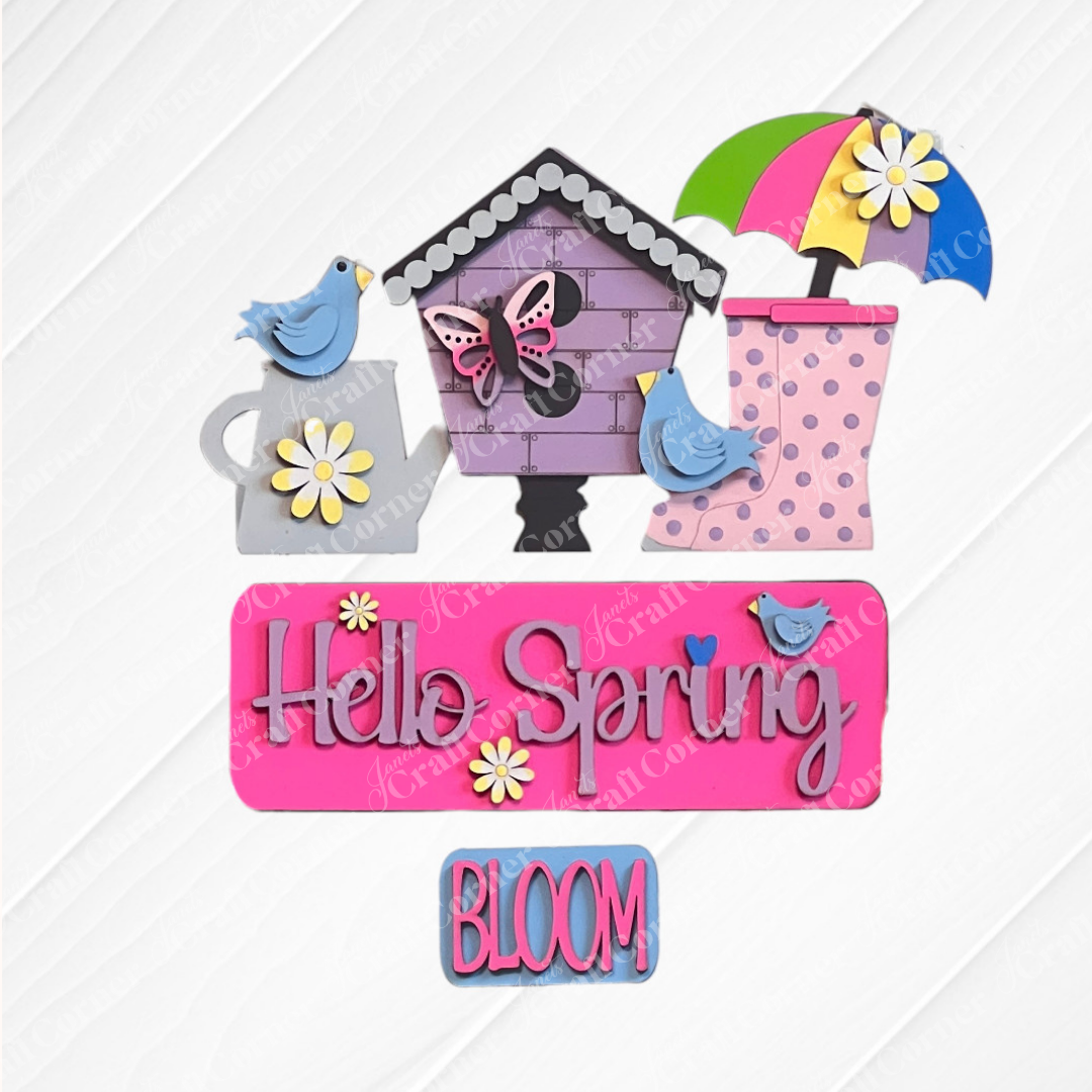 Complete your textured surface with vibrant spring-themed decorations from Janet's Craft Corner. The scene includes a birdhouse, bluebirds, an umbrella, and rain boots. A charming sign displays "Hello Spring" in purple adorned with flowers. This delightful setup is part of the Hello Spring Interchangeable Insert DIY home decor kit, featuring an additional option that says "BLOOM.