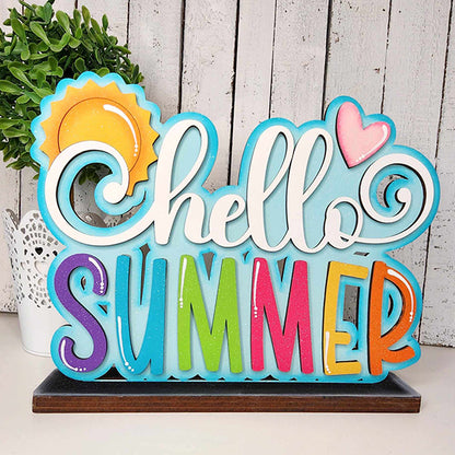 The "Hello Summer Standing Shelf Sitter" by Janet's Craft Corner is an ideal addition to your summer decor, featuring a vibrant "Hello" in white accompanied by sun and heart designs, and "Summer" illuminated with multicolored letters. This delightful DIY kit stands on a wooden surface, surrounded by lush greenery.