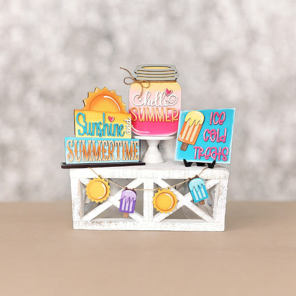 Create a charming summer display with Janet's Craft Corner's Hello Summer Tiered Tray Set, featuring a decorative wooden crate filled with delightful signs and cutouts. The set includes images of a sun, ice cream, and a mason jar labeled "Hello Summer." Enjoy the playful signs that read "Sunshine and Summertime" and "Ice Cold Treats," complemented by small banners of suns and popsicles for the perfect seasonal decor.