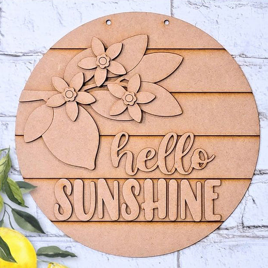 The Hello Sunshine Lemon Round Sign from Janet's Craft Corner is a charming wooden décor piece featuring cut-out flowers and leaves with "hello SUNSHINE" hand-painted on it. It complements a light brick wall adorned with lemons and lush green leaves, perfect for home decoration.