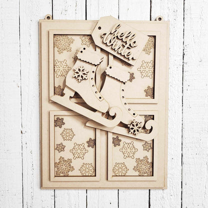 The Hello Winter Window Hanger by Janet's Craft Corner is a DIY seasonal home decor kit featuring ice skates with snowflake cutouts and a "hello winter" tag, set against etched snowflakes on a white wooden wall.