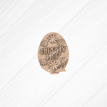 Easter Trio Mini Shelf Sitters by Janet's Craft Corner feature wooden egg cutouts with "Hippity Hop" and flower designs, ideal for adding cheer to your Easter decor or as shelf sitters. This decoration set includes a stand and an extra grass-shaped piece, all set against a textured, light background.