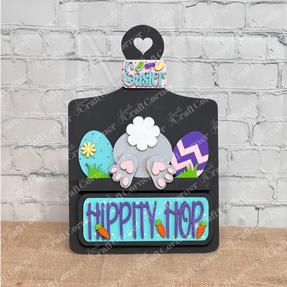 The "Hippity Hop Bunny Butt Interchangeable Insert" by Janet's Craft Corner features a decorative bunny rear with Easter eggs. The "Hippity Hop" sign is perfect home decor against a white brick wall for a festive touch.