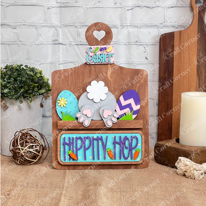 The "Hippity Hop Bunny Butt Interchangeable Insert" by Janet's Craft Corner features a decorative bunny rear with Easter eggs. The "Hippity Hop" sign is perfect home decor shown on a stained decorative breadboard against a white brick wall for a festive touch.