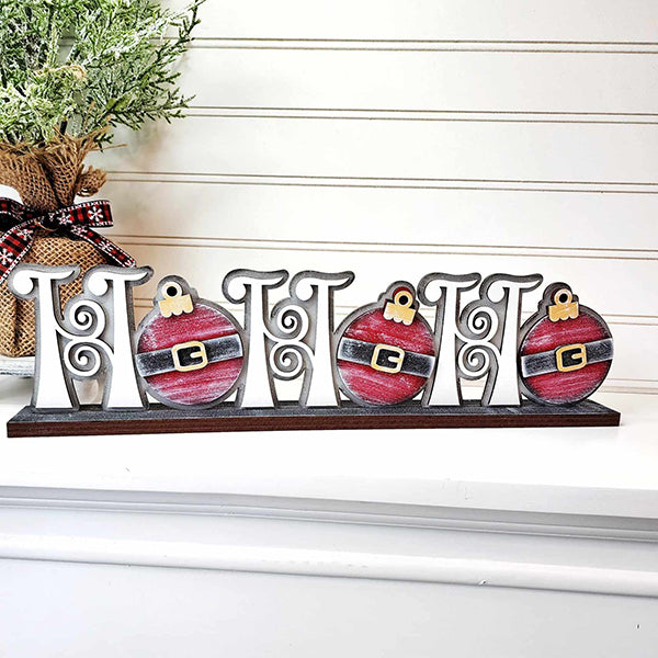 This Ho Ho Ho Shelf Sitter from Janet's Craft Corner displays decorative "O"s designed like Santa belts, bringing a playful element to your personalized home décor. In the background, a potted plant wrapped in burlap and ribbon beautifully completes the festive scene.