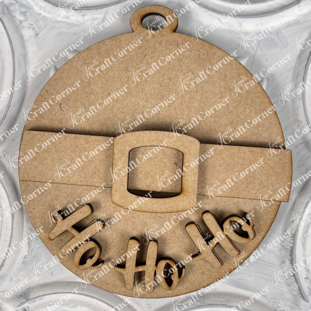 A charming Christmas ornament from Janet's Craft Corner, this piece is a round wooden design resembling Santa's belt, featuring "Ho Ho Ho" cut out at the bottom. Ideal for enhancing your home décor, it makes a striking contrast against a textured white surface adorned with circular patterns.
