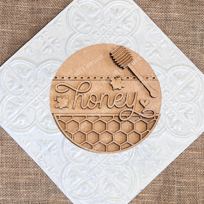 The Honey Bee Mini Shelf Sitters by Janet's Craft Corner is a DIY decor kit featuring a round wooden plaque with "honey" in cursive, bee and heart accents, a honey dipper, and honeycomb design—perfect for seasonal home decorating.