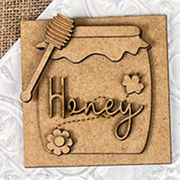 The Bee Swappable Squares from Janet's Craft Corner feature a honey jar design with "Honey" in cursive, plus flower and bee details, adding handmade charm to your decor on a white and burlap background.