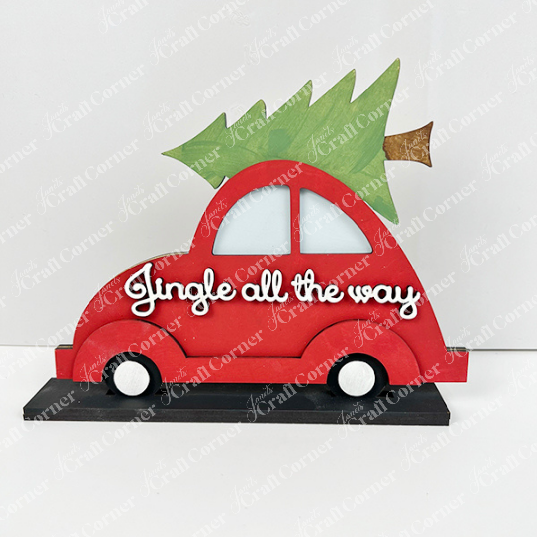 The Jingle All the Way Volkswagen Shelf Sitter by Janet's Craft Corner is a decorative piece featuring a red Volkswagen car with an evergreen tree on top, embellished with the phrase "Jingle all the way" in white script, perfectly capturing the spirit of yuletide cheer. The car is showcased against a plain white backdrop.