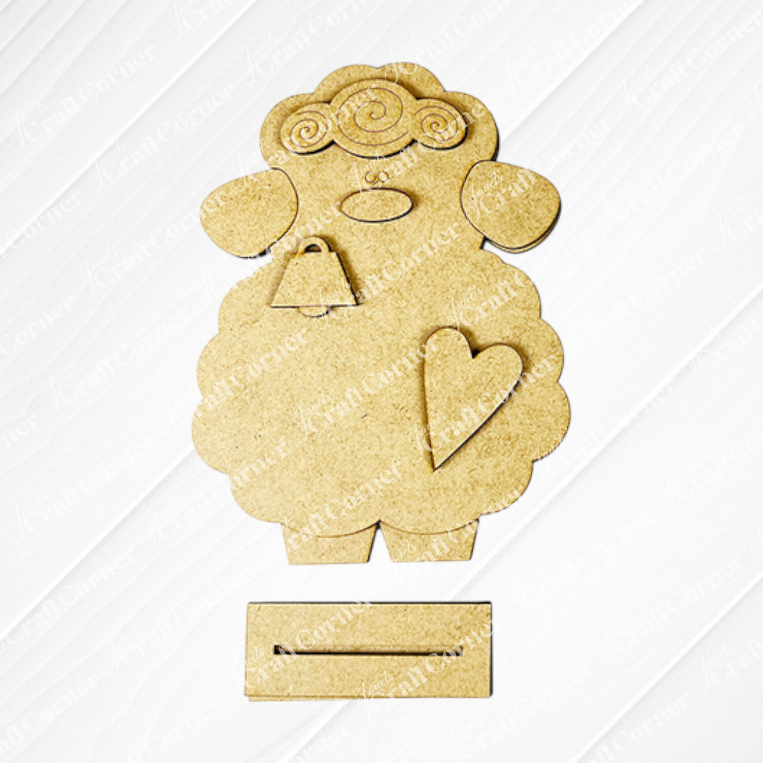 Janet's Craft Corner offers a Lamb Shelf Sitter DIY Kit featuring a charming wooden sheep cutout with curly wool, facial details, a heart on each body, and bottom slots. Shown against a white background—ideal as home décor!.