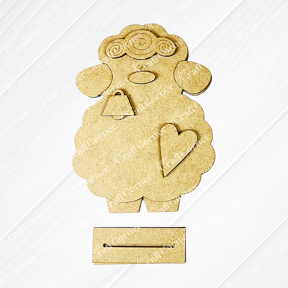 Janet's Craft Corner offers a Lamb Shelf Sitter DIY Kit featuring a charming wooden sheep cutout with curly wool, facial details, a heart on each body, and bottom slots. Shown against a white background—ideal as home décor!.