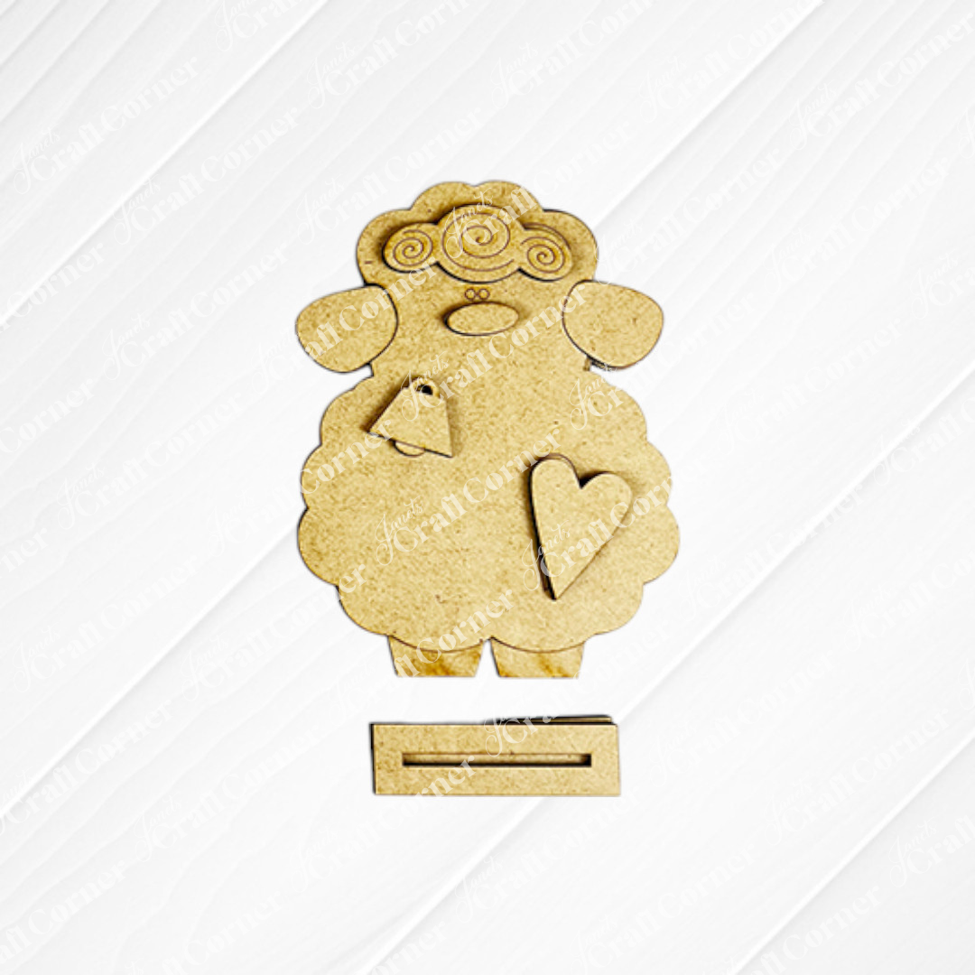 Janet's Craft Corner offers a Lamb Shelf Sitter DIY Kit featuring a charming wooden sheep cutout with curly wool, facial details, a heart on each body, and bottom slots. Shown against a white background—ideal as home décor!.