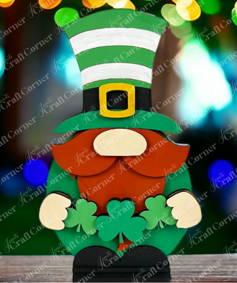 Janet's Craft Corner offers a Leprechaun Gnome Shelf Sitter DIY kit. This whimsical wooden figure has an orange beard, green clothes, a striped hat, and holds three shamrocks. A festive décor piece that brightens any space with its charm! Ideal for those who love holiday cheer.