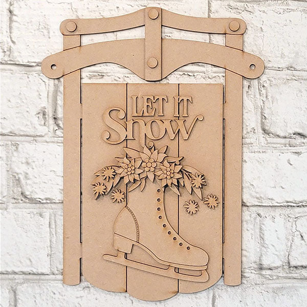 Janet's Craft Corner's "Let It Snow Sled Sign" DIY kit includes a wooden sled wall decoration featuring an ice skate with floral accents and the text "Let It Snow" against a white brick wall backdrop, ideal for seasonal styling and crafting enthusiasts.