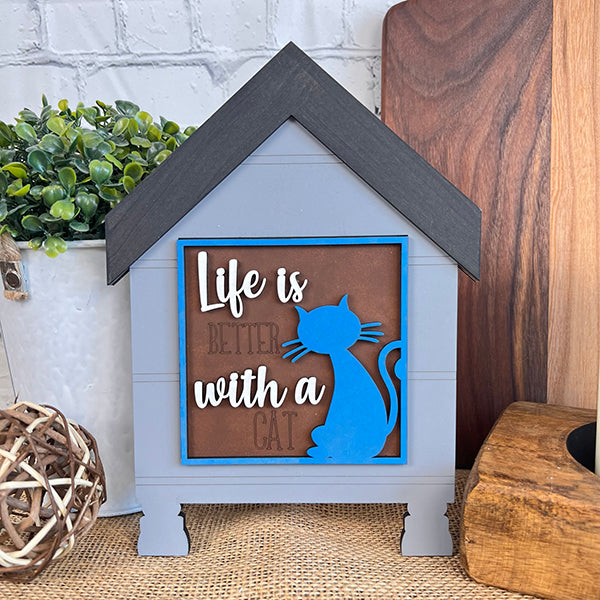 Janet's Craft Corner Cat Swappable Squares is a wooden house-shaped sign with "Life is better with a cat," a blue cat silhouette, plants, and boards—perfect for DIY seasonal home decor and craft projects.