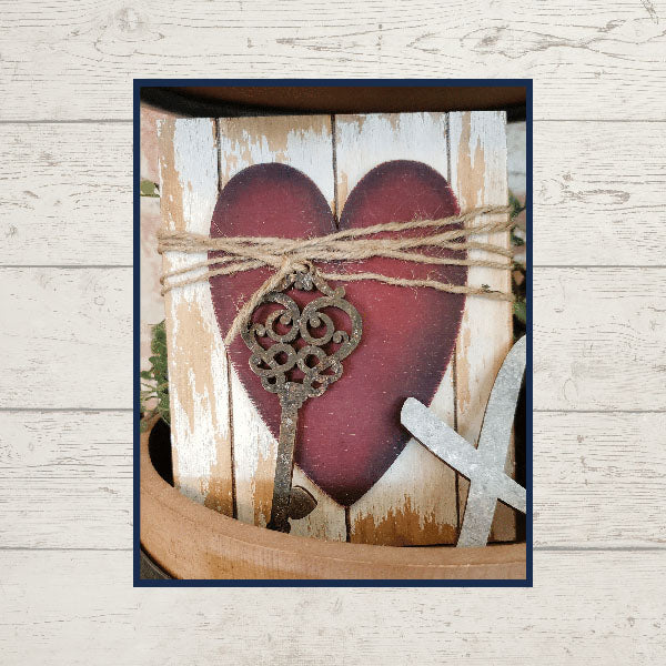 Introducing the "Love Lives Here Decor Set" by Janet's Craft Corner: This charming rustic wall decoration kit is ideal for bringing a touch of elegance to your home décor. It features a large red-painted wooden heart, wrapped with twine and adorned with an ornate key, perfectly complementing any tiered tray display against its weathered wooden background.