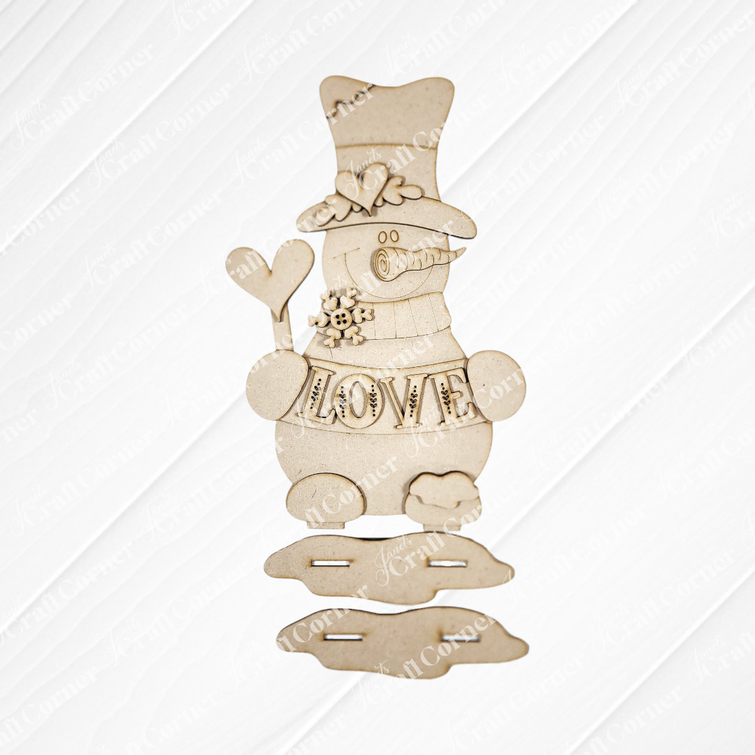 The Love Snowman Shelf Sitter DIY kit by Janet's Craft Corner features a wooden snowman with top hat, scarf, heart-shaped arm, and "LOVE" across the middle—perfect as a charming handmade gift or seasonal home decor. Set of 1.