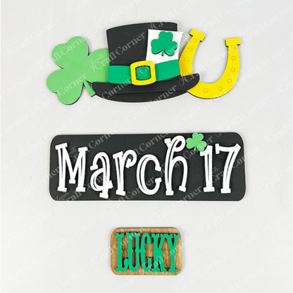 Celebrate St. Patrick's Day with Janet's Craft Corner's March 17 Interchangeable Insert DIY home decor kit, highlighting a black hat decorated with green shamrocks and a yellow horseshoe, a charming sign that reads "March 17," and a versatile wooden block showcasing "Lucky" in bold green letters.