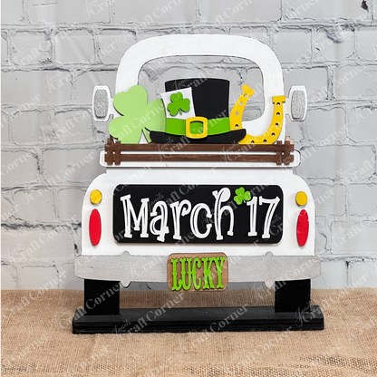 The "March 17 Interchangeable Insert" from Janet's Craft Corner is a decorative piece designed to resemble the back of a truck, perfect for celebrating St. Patrick's Day. It features symbols like a shamrock, leprechaun hat, and horseshoe, along with the date "March 17." With "LUCKY" displayed on the license plate, this DIY home decor kit makes an ideal piece of interchangeable home decor against a white brick wall.