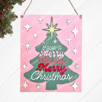 Janet's Craft Corner "Have a Merry Christmas Tree" Wall Hanger is a DIY seasonal home decor craft kit featuring a green tree shape on a pink background with white stars and "Have a Merry Merry Merry Christmas" in red and white script. Set of 1.