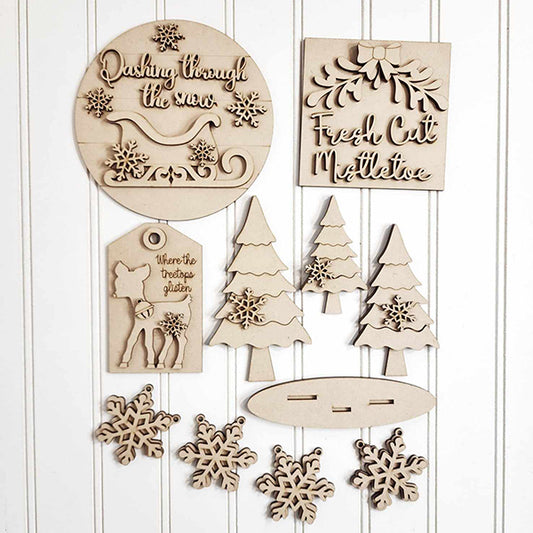 Explore the Mistletoe Tiered Tray DIY Decor Kit by Janet's Craft Corner—a charming set of five wooden decorations featuring winter-themed designs like snowflakes, trees, sleighs, and reindeer. Each piece is adorned with festive phrases such as "Dashing through the snow" and "Fresh Cut Mistletoe," making them a perfect addition to any white background.