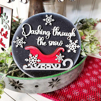 The Mistletoe Tiered Tray DIY Decor Kit from Janet's Craft Corner includes a hand-painted decorative sign with "Dashing through the snow" in white script, featuring a red sleigh, white snowflakes, and mistletoe. It's the perfect holiday decor when displayed on a metal tray with a red cloth beneath.