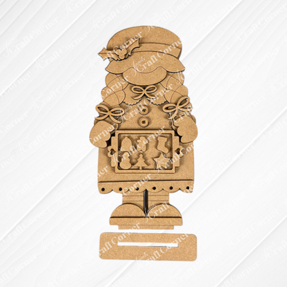 Janet's Craft Corner offers the Mrs Claus Baking Gnome Shelf Sitter, a charming wooden figure donning a hat and holly. Holding a plaque with festive shapes, it's perfect for your holiday display, set on a textured white background on burlap. This DIY seasonal home decor craft kit comes as a set of 1.