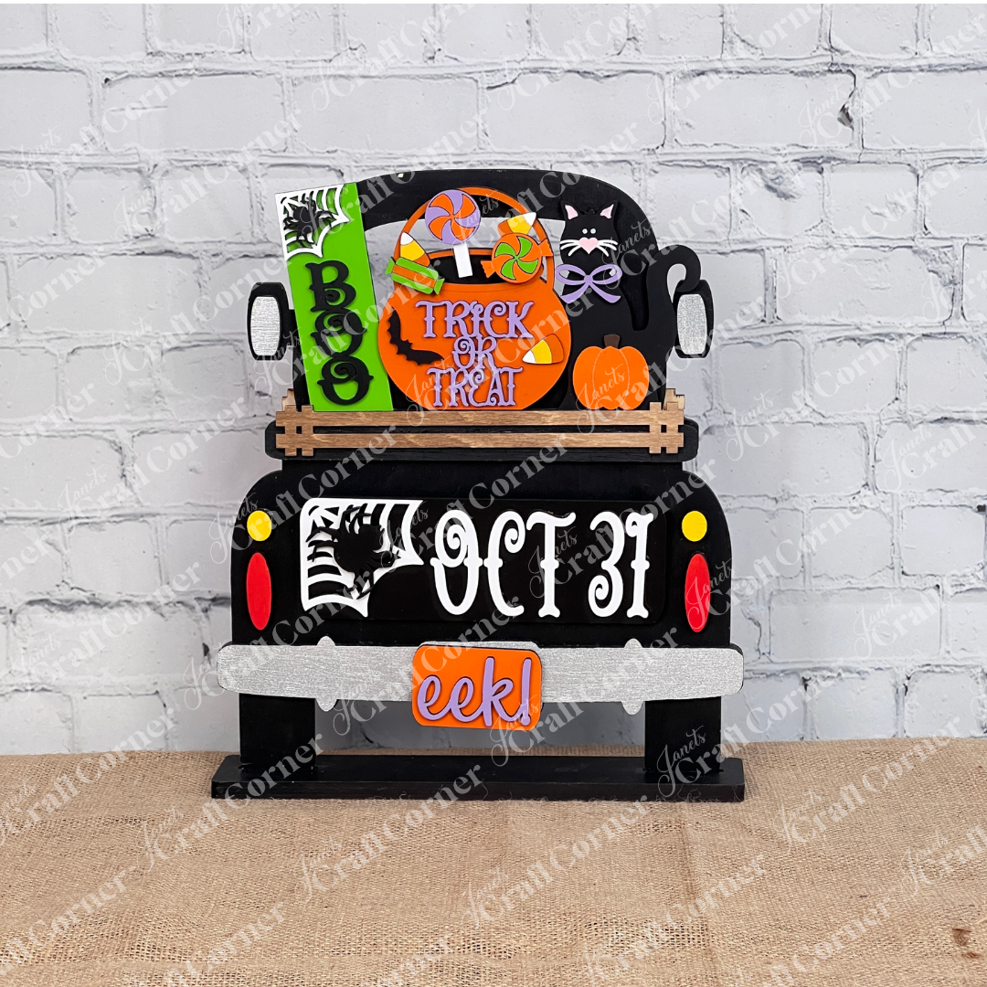 An enchanting Halloween-themed display depicts the rear of a truck adorned with vibrant signs that say "Boo," "Trick or Treat," and "Oct 31." This DIY craft kit from Janet's Craft Corner, named the Oct 31 Interchangeable Insert, features hand-painted elements including candies, a black cat with a pumpkin, and other festive decorations—ideal for creating versatile home decor.