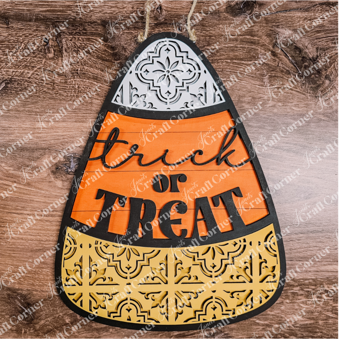 Decorative Halloween candy corn sign with 'Trick or Treat' text on a wooden background.