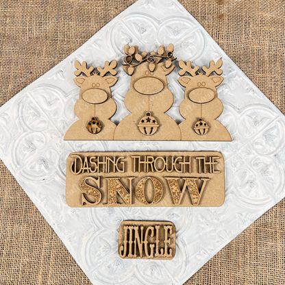 The Reindeer Interchangeable Insert from Janet's Craft Corner features three antlered reindeer set against a textured burlap background, with signs that read "Dashing Through the Snow" and "Jingle." As a DIY home decor kit, it is perfect for adding festive charm to any space.