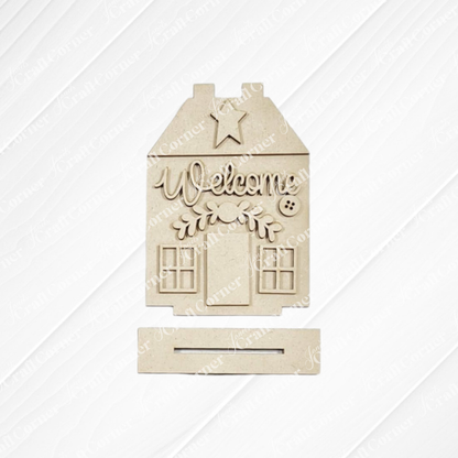 Janet's Craft Corner Heirloom Decor Set is a DIY seasonal home decor kit shaped like a house with "Welcome," decorative branches, star, and window details. The rectangular base has a slot, making it perfect for any space. Choose from 5 unique designs.