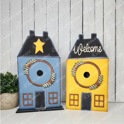 Janet's Craft Corner Saltbox House Round Display DIY kit features a charming saltbox house design with a blue star or “Welcome” sign option, plus wreaths and window details—perfect for creating seasonal home décor. Set of 1.