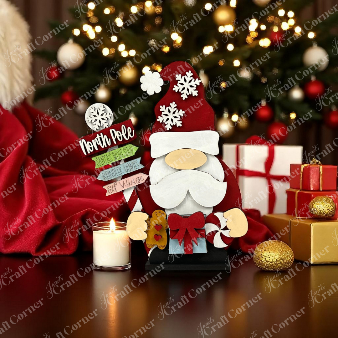 The Santa Gnome Shelf Sitter from Janet's Craft Corner, a DIY seasonal home decor craft kit,  sits on a table with festive accents and a decorated Christmas tree in the background.