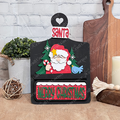 The Santa Merry Christmas Interchangeable Insert DIY craft kit by Janet's Craft Corner includes 3 decorative pieces. Featuring festive colors and a cutout heart, it's perfect for brightening your kitchen counter this holiday season.