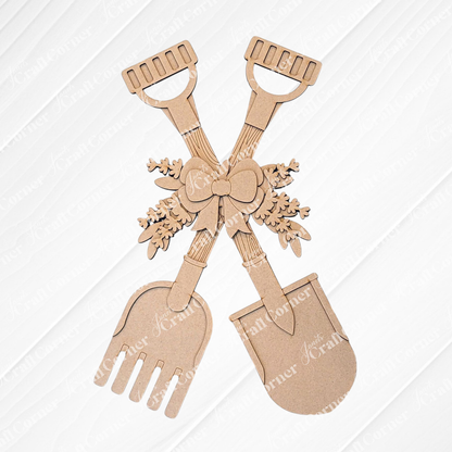The Shovel and Rake Door Hanger by Janet's Craft Corner features two crossed gardening tools against a white brick wall, with bows and leaves accents. This DIY craft kit is ideal for a paint-it-yourself project or as a charming addition to rustic wood decor.