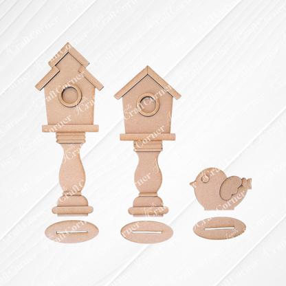 Displayed against white wood, the Spindle Birdhouses Shelf Sitter by Janet's Craft Corner includes two birdhouse cutouts and a bird cutout on pedestals. This DIY kit features slots for interlocking, offering a simple, unfinished design perfect for charming shelf sitters.