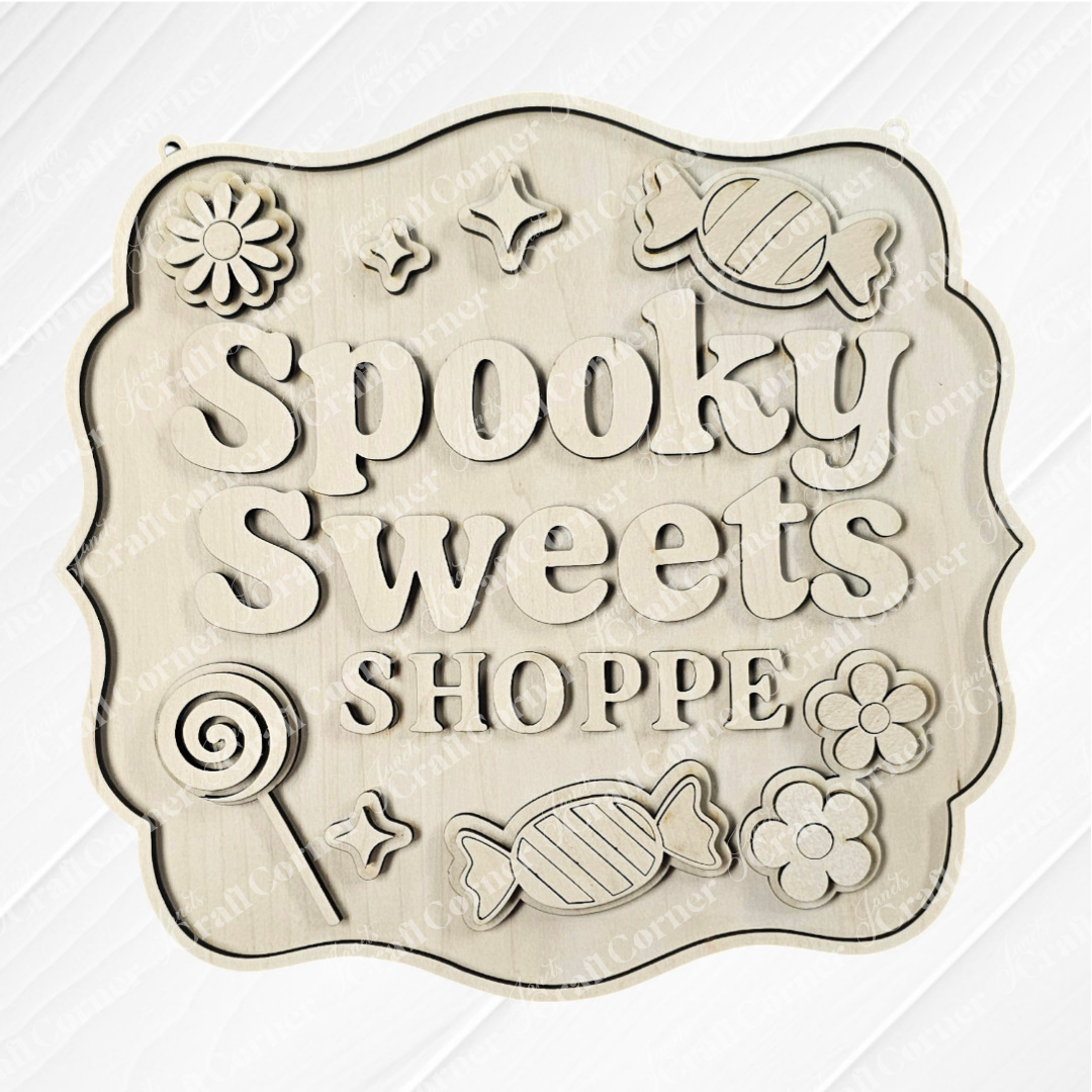 The Spooky Sweets Shoppe Wall Hanger by Janet's Craft Corner features candy, flower, lollipop, and spider web carvings on light wood—ideal as seasonal home decor or a DIY wall hanger.
