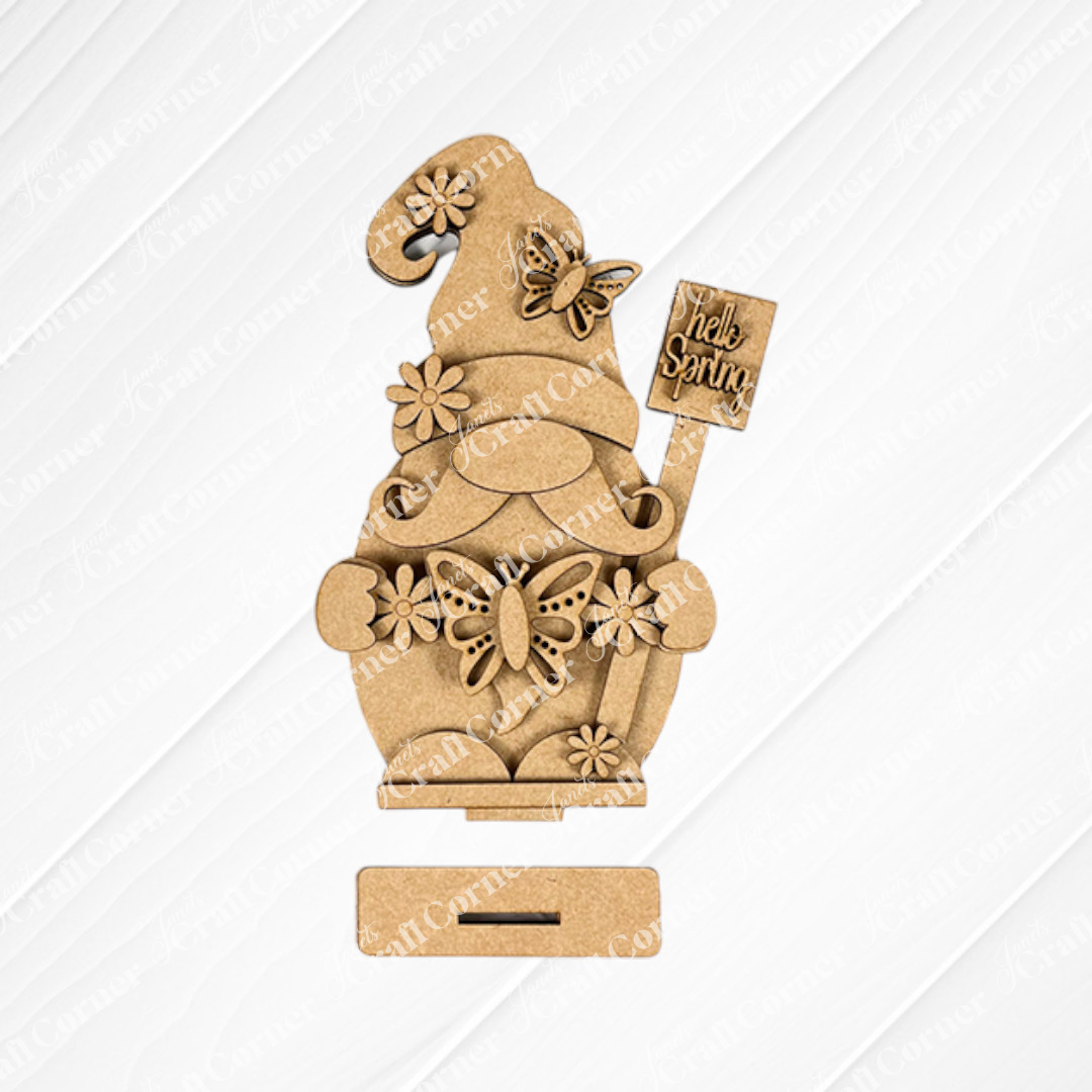 The Spring Butterfly Gnome Shelf Sitter from Janet's Craft Corner is a DIY craft kit featuring a gnome holding a "Hello Spring" sign. Ideal for home décor, it includes floral and butterfly accents on a textured white background with a base slot.