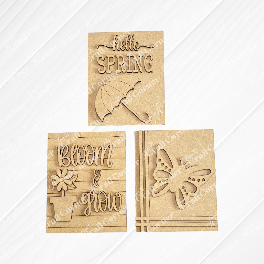 Janet's Craft Corner Spring Switchable Farmhouse Signs DIY Kit includes three brown cut-out wooden plaques: "hello SPRING" with an umbrella, "bloom & grow" with a flower pot, and a butterfly—perfect for spring tiered tray decor.