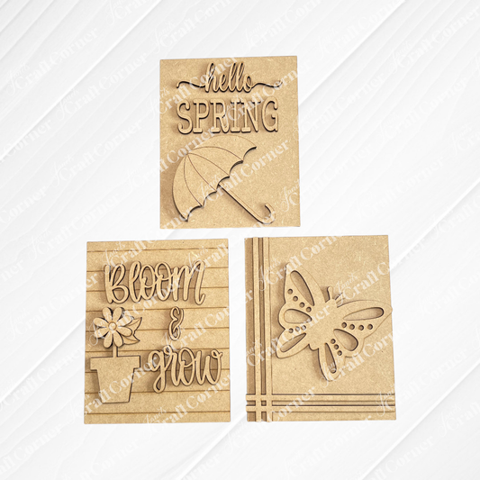Janet's Craft Corner Spring Switchable Farmhouse Signs DIY Kit includes three brown cut-out wooden plaques: "hello SPRING" with an umbrella, "bloom & grow" with a flower pot, and a butterfly—perfect for spring tiered tray decor.