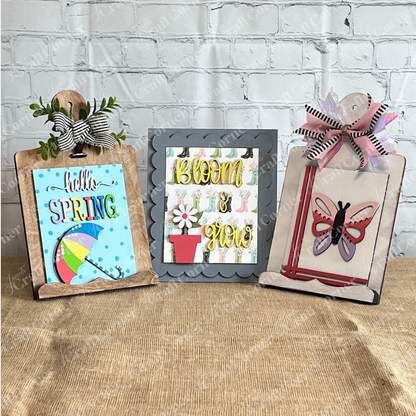 Janet's Craft Corner Spring Switchable Farmhouse Signs DIY Kit includes three clipboard-style wood signs: "hello SPRING" with umbrella, "Bloom & grow" with flower pot, and a butterfly—each rustic with bows, ideal for tiered trays or craft projects.