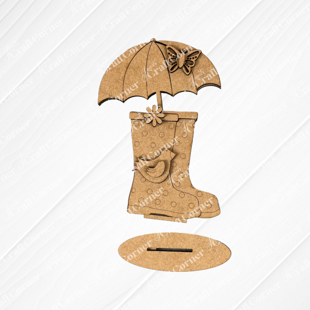 Introducing the "Spring Standing Signs" from Janet's Craft Corner—a decorative wooden cutout that showcases rain boots adorned with a delicate flower, topped with an umbrella and butterfly. Set against a white wooden background, it's an ideal choice for either a welcoming spring display or an enchanting DIY home décor project.