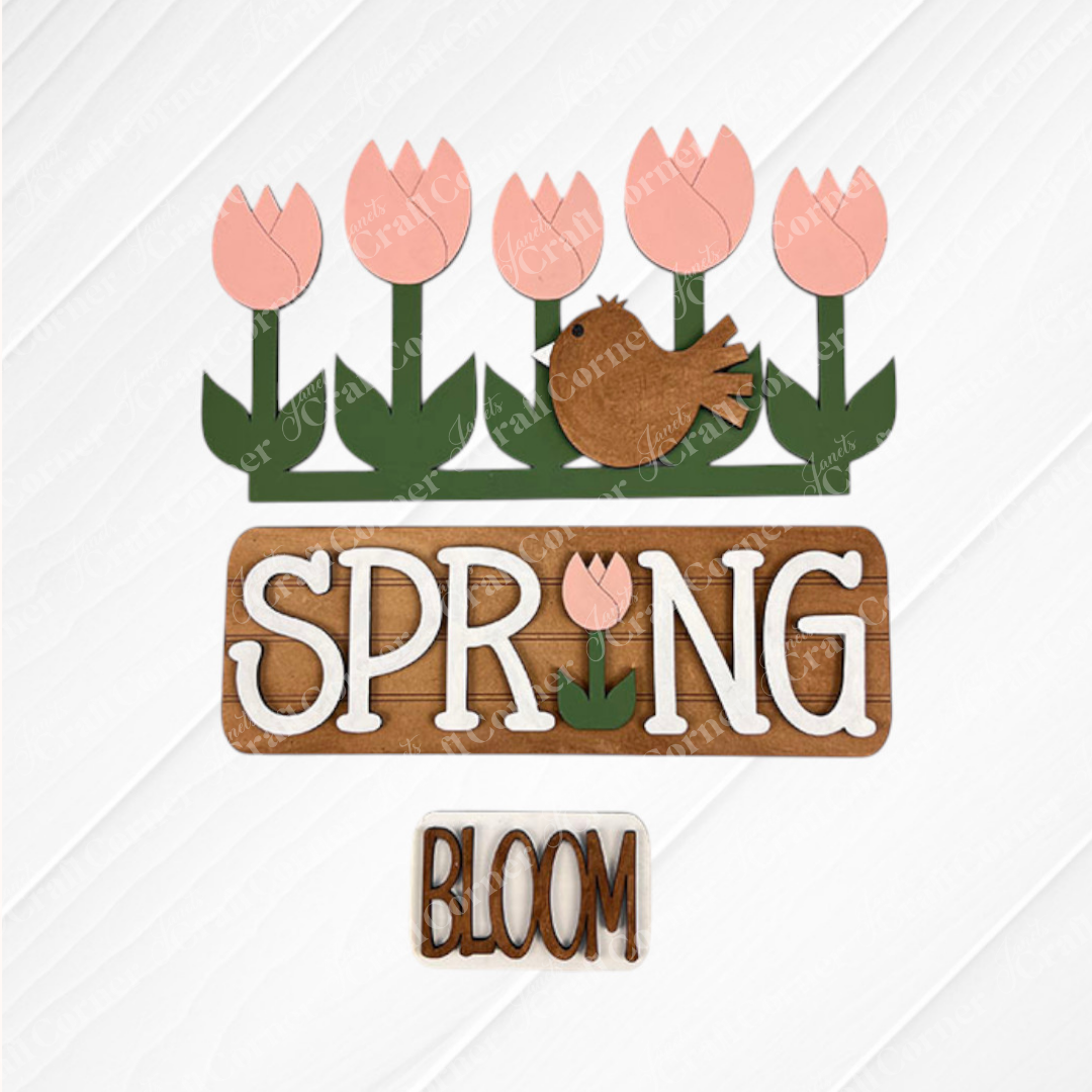 Introducing the "Spring Tulips Interchangeable Insert" from Janet's Craft Corner – a DIY home decor kit that showcases a delightful spring-themed design. This artwork features pink tulips and a brown bird set against a white background, with the word "SPRING" prominently displayed and cleverly incorporating a tulip for the letter "I." A smaller accompanying sign reads "BLOOM.