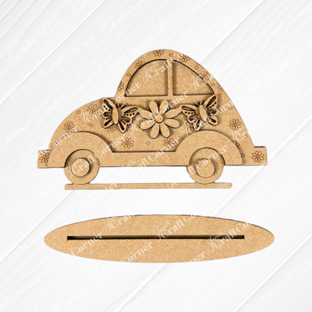 Janet's Craft Corner offers the Spring Volkswagen Shelf Sitter— a DIY decorative piece. This wooden car-shaped decor, featuring floral and butterfly designs, rests on a textured white square atop burlap with an oval wooden stand below, perfect for any home décor collection.