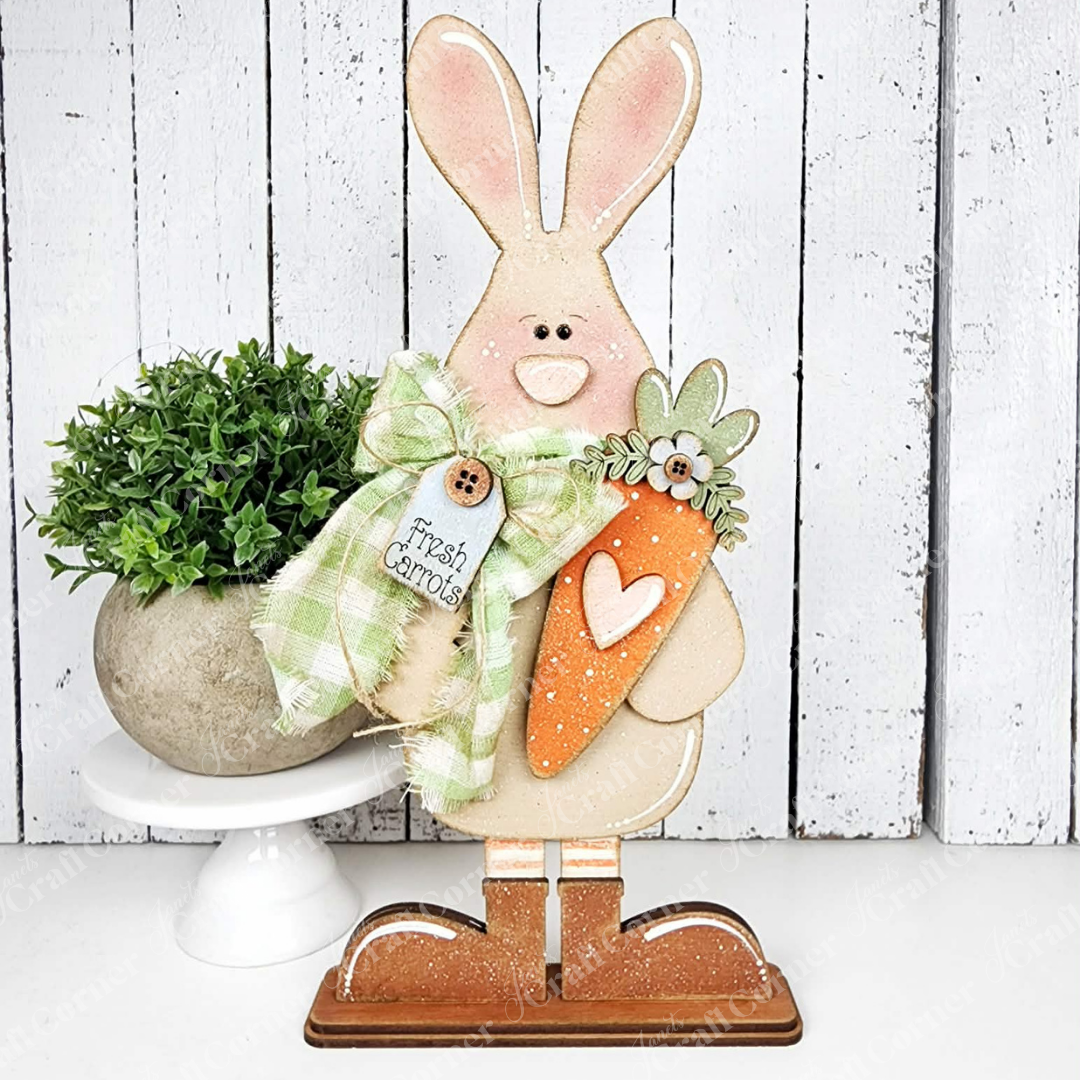 Add a charming touch to spring with Janet's Craft Corner Standing Carrot Bunny Shelf Sitter DIY kit—includes a bunny figurine holding an orange carrot and heart, with a green plaid bow labeled "Fresh Carrots." Set of 1.