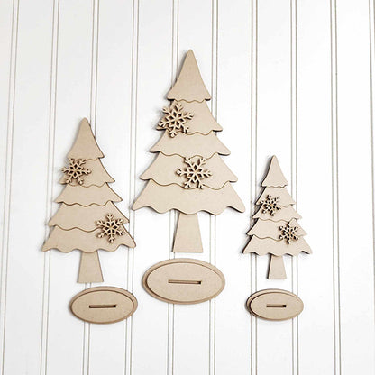 Bring a personalized touch to your home décor with Janet's Craft Corner's "Standing Trees - Set of 3" DIY Home Decor Craft Kit. Featuring three wooden Christmas tree cutouts in different sizes, each adorned with decorative snowflakes, these trees sit on an oval base and are set against a white paneled background.