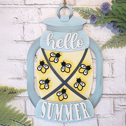 Add a touch of charming farmhouse style to your home decor with the Summer Lantern Door Hanger from Janet's Craft Corner. This decorative wooden sign, shaped like a lantern and featuring the words "hello summer," showcases cute bees and a cheerful yellow background. Perfect for gracing a white brick wall, it's beautifully complemented by vibrant greenery.