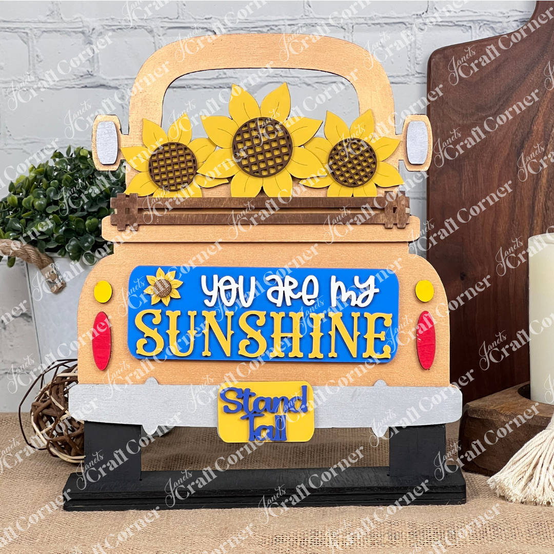 The Sunflower Interchangeable Insert from Janet's Craft Corner is a DIY home decor kit featuring a wooden truck cutout adorned with sunflowers and the phrase "You Are My Sunshine" in yellow and white, plus a small "Stand Tall" tag. Ideal for fans of interchangeable decorations, it complements any setting with plants, candles, or cutting boards.