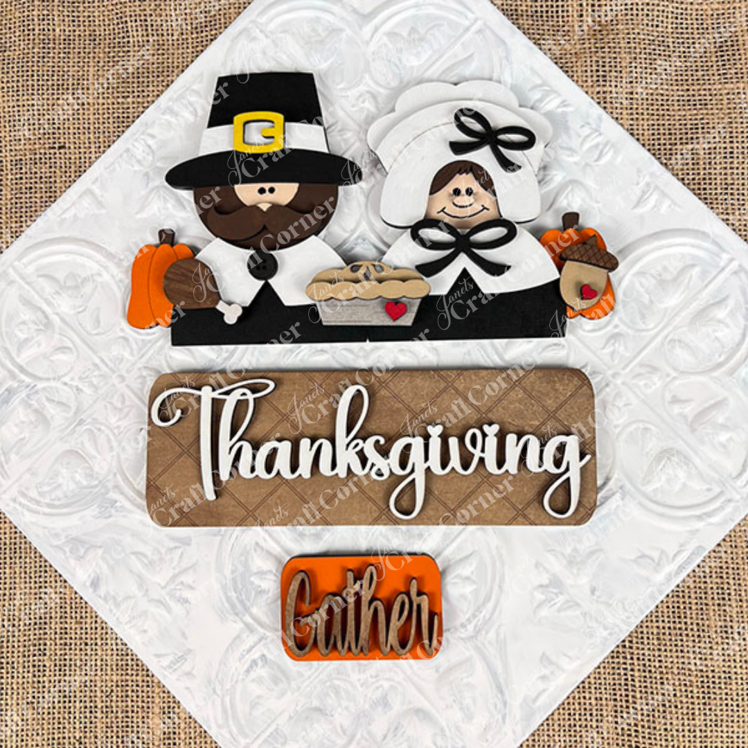 The Pilgrim Interchangeable Insert from Janet's Craft Corner is a DIY home decor kit that features a decorative design with a pilgrim couple, pumpkins, a pie, and an acorn. The word "Thanksgiving" is prominently displayed with "Gather" beneath it on a burlap-textured background, ideal for refreshing your Thanksgiving decor or creating unique craft projects.